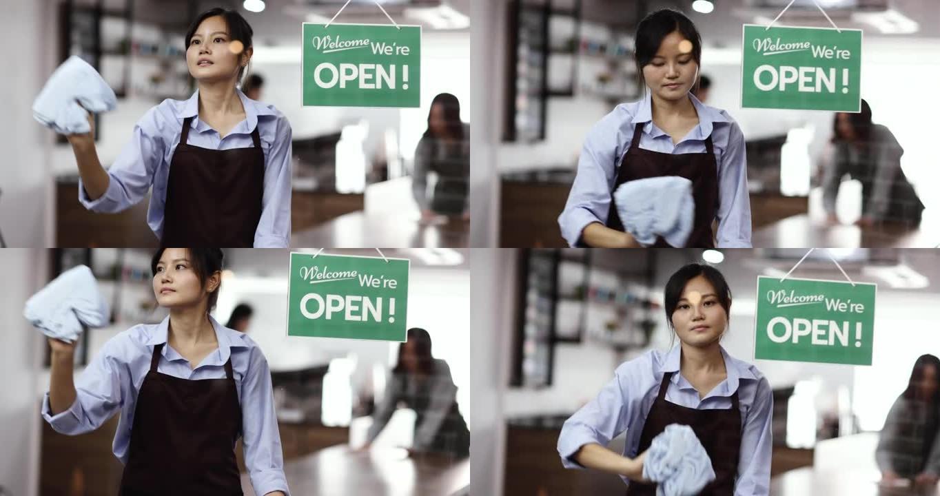 中式风格的年轻女性咖啡店老板用衣服擦拭和清洁咖啡馆前门的透明玻璃墙，然后打开为客户服务，背景是团队清