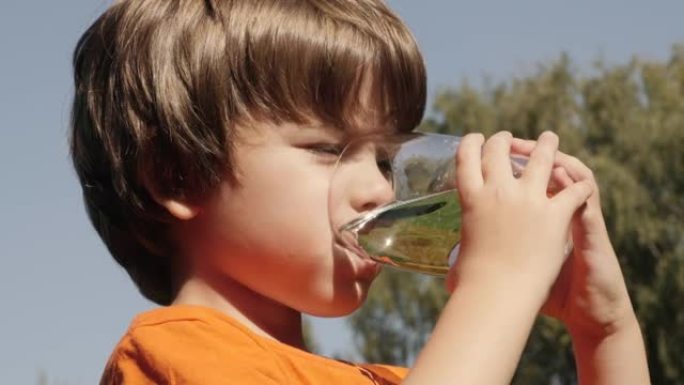 口渴的孩子在户外用玻璃喝水，阳光普照。男童水杯新鲜透明纯净水慢动作儿童水杯水健康身体护理健康生活方式
