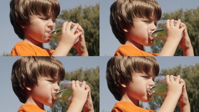 口渴的孩子在户外用玻璃喝水，阳光普照。男童水杯新鲜透明纯净水慢动作儿童水杯水健康身体护理健康生活方式