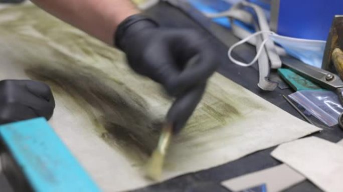 在工艺品修理店的工作台上用刷子将胶水涂在皮片上