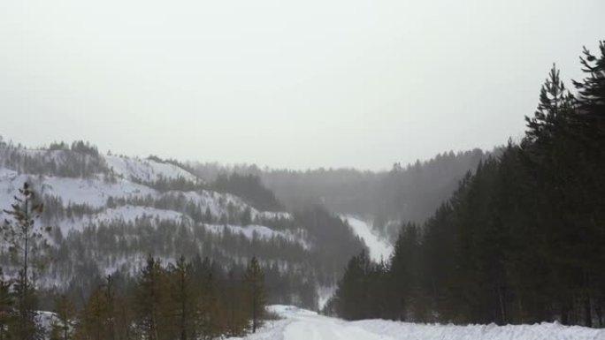 在阴天的冬日，在山腰上查看冬季道路。镜头。冬季旧采石场沿路径的暴风雪的第一人称视角