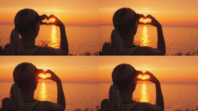一个女人看着太阳落山的大海，显示出一个心形的身影