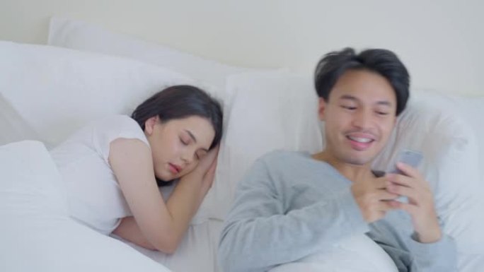 亚洲迷人的搞笑男性自拍，床上熟睡的女朋友。幸福的家庭，新婚的男人和女人一起度过早晨的时间丈夫躺在卧室