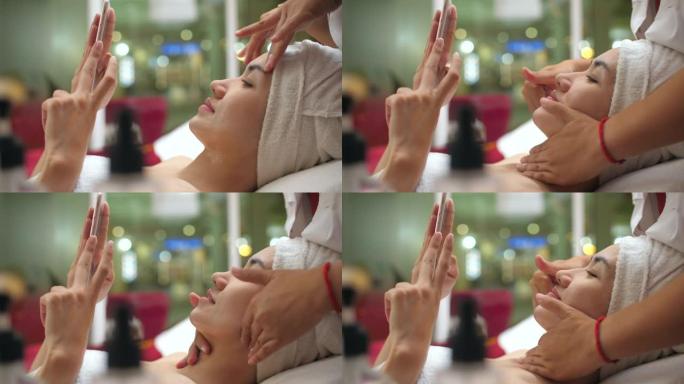 亚洲女性在水疗中心进行面部按摩时在智能手机上放松
