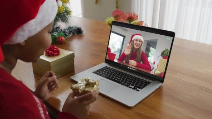 戴着圣诞老人帽子的非裔美国妇女使用笔记本电脑进行圣诞节视频通话，屏幕上有妇女