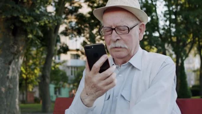 体贴的戴眼镜的老人在公园的手机摄像头上认真聊天