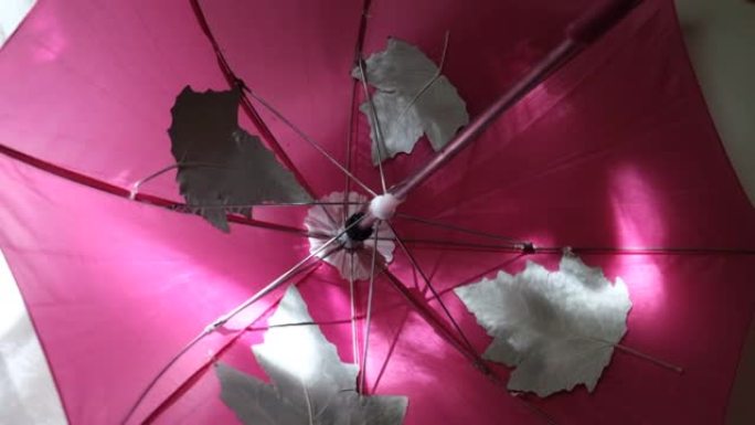 秋季背景与旋转粉色雨伞特写。孩子打伞，在家玩