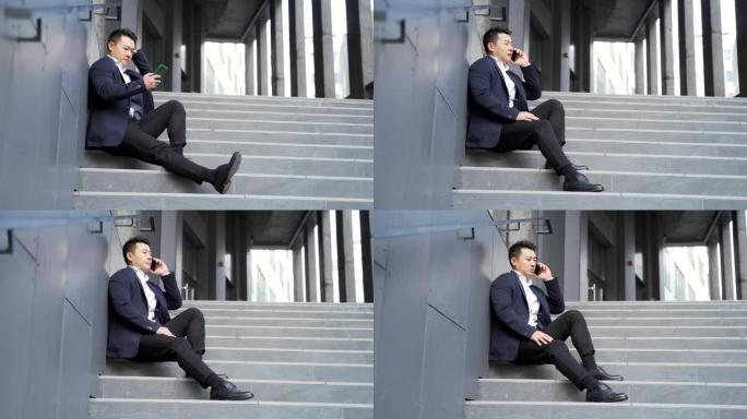 年轻的亚洲沮丧男子坐在办公室商务中心大楼附近的楼梯户外街道上