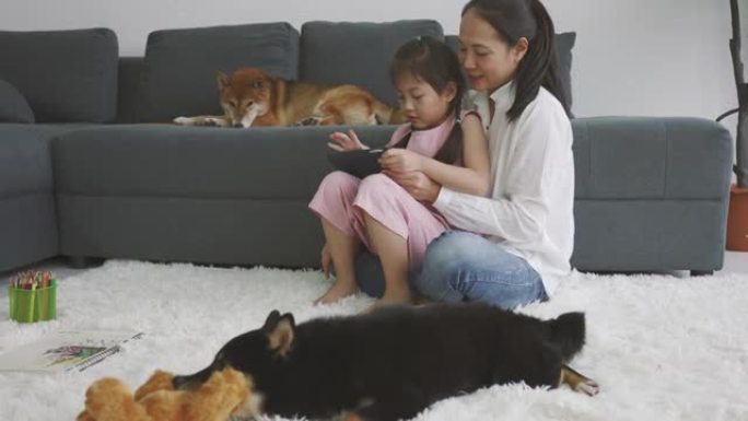 亚洲母女使用数字平板电脑与狗一起学习。家庭在室内休息。