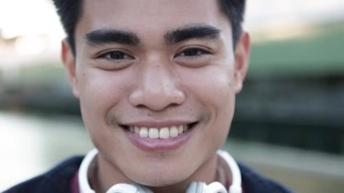 戴着耳机对着镜头微笑的英俊年轻亚洲男子的特写肖像