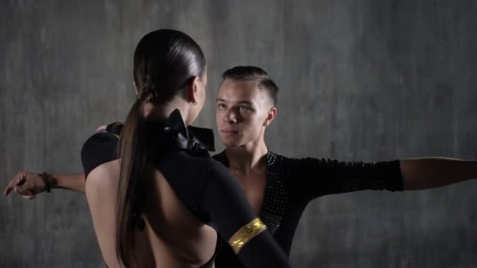 这对年轻的千禧一代舞蹈夫妇穿着黑色连衣裙，在工作室背景下以性感的姿势跳舞。