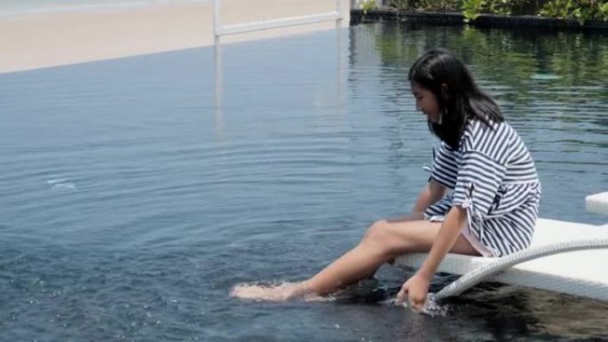 快乐的亚洲女孩在度假期间在酒店游泳池附近的日光浴床上放松时泼水，生活方式理念。