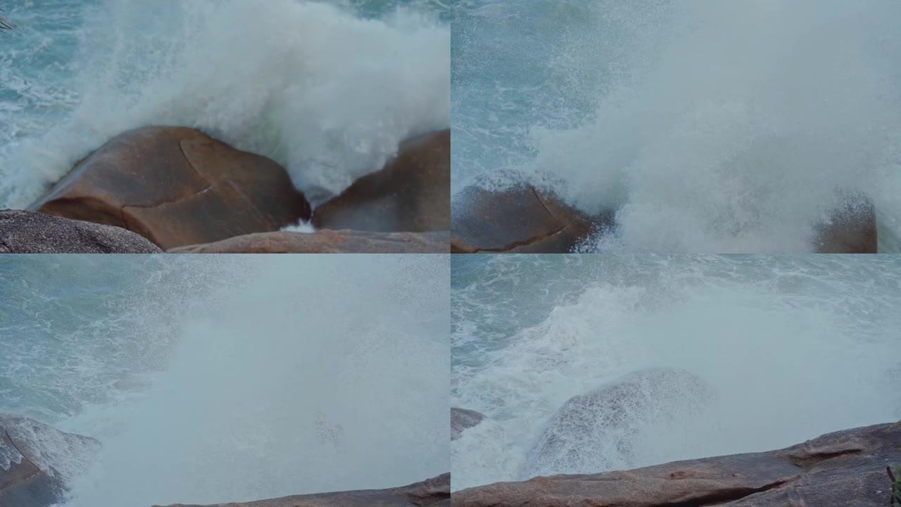 强大的海浪溅到海中的一块大石头上。在岩石热带海岸附近的岩石上冒泡的猛烈破浪