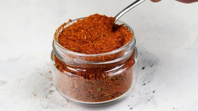 厨师从玻璃香料罐中取出茶匙香料磨碎的红辣椒或辣椒。