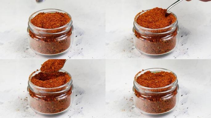 厨师从玻璃香料罐中取出茶匙香料磨碎的红辣椒或辣椒。