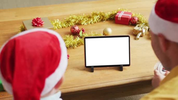 高加索人的父亲和儿子戴着圣诞老人的帽子，进行平板电脑圣诞节视频通话，在屏幕上复制空间