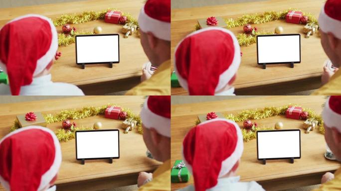 高加索人的父亲和儿子戴着圣诞老人的帽子，进行平板电脑圣诞节视频通话，在屏幕上复制空间