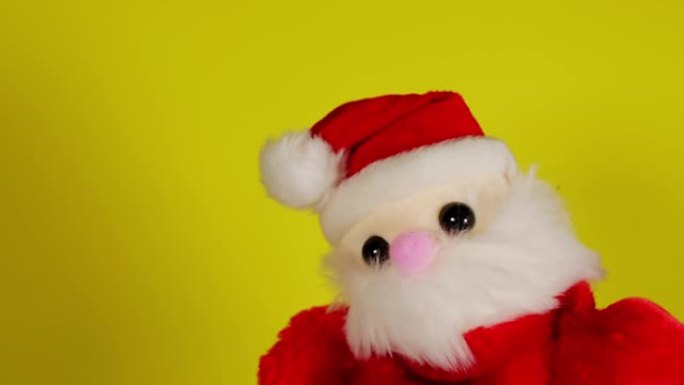 黄色背景上圣诞老人的毛绒玩具。手边圣诞老人木偶的特写。布袋戏的概念和即将到来的新年假期