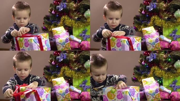 坐在圣诞树下的好奇小男孩解开礼品盒上的丝带。圣诞节。