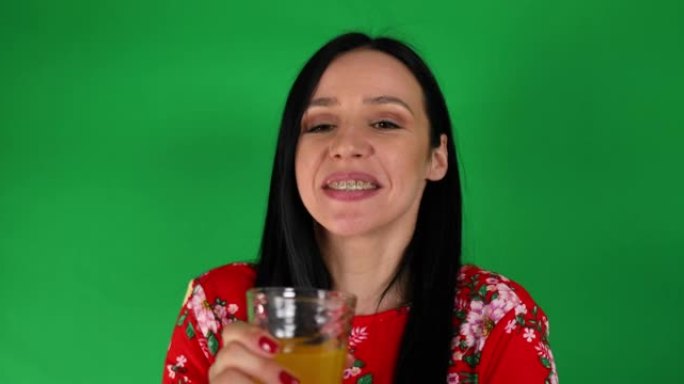 女人从绿色背景前的酒杯中喝橙色汽水