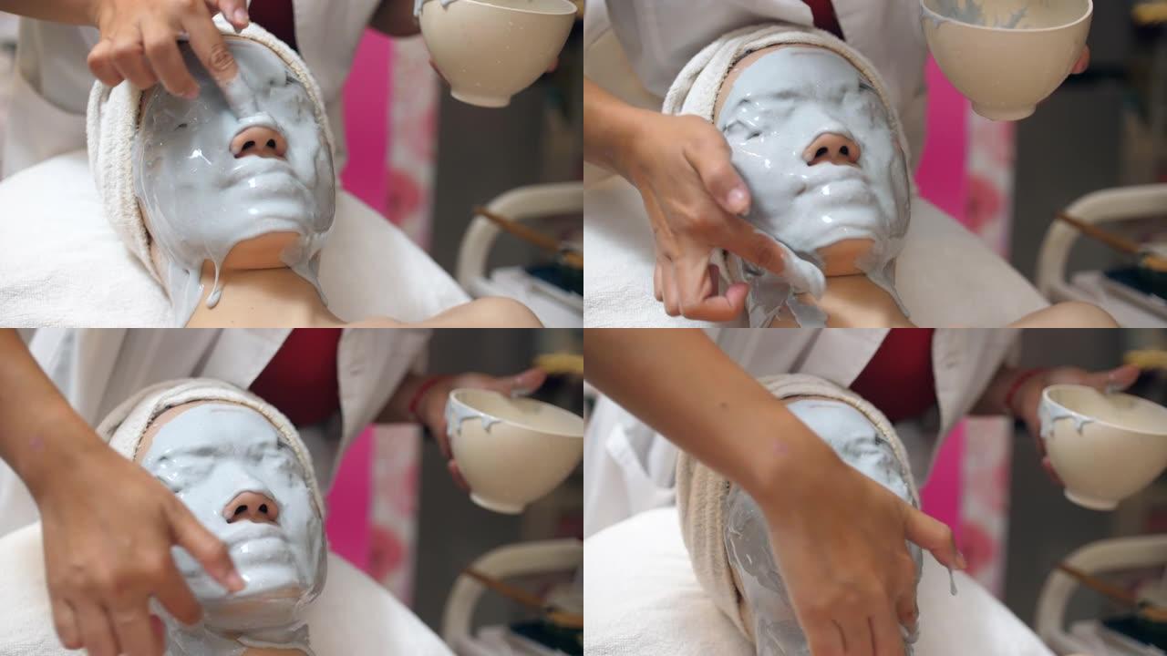 年轻的亚洲妇女在水疗中心使用带有头部按摩的维生素面膜