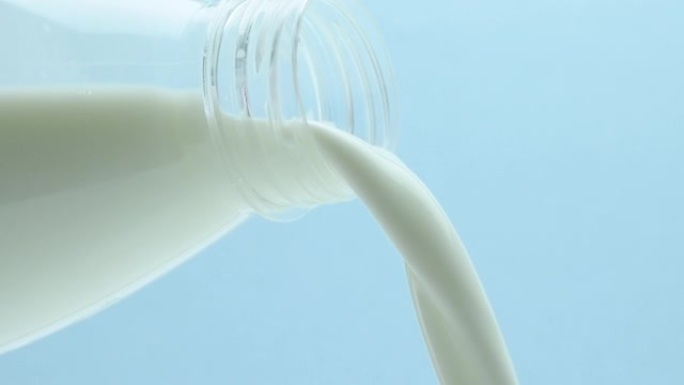 从塑料瓶中倒牛奶特写，在蓝色背景上
