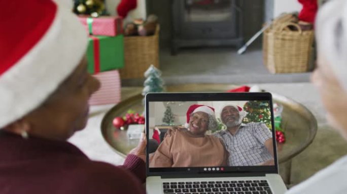 微笑着的资深女性朋友使用笔记本电脑与屏幕上的情侣进行圣诞节视频通话