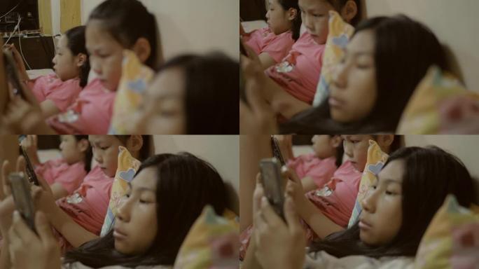 亚洲儿童使用数字平板电脑和手机，同时在家一起在床上放松，生活方式理念。