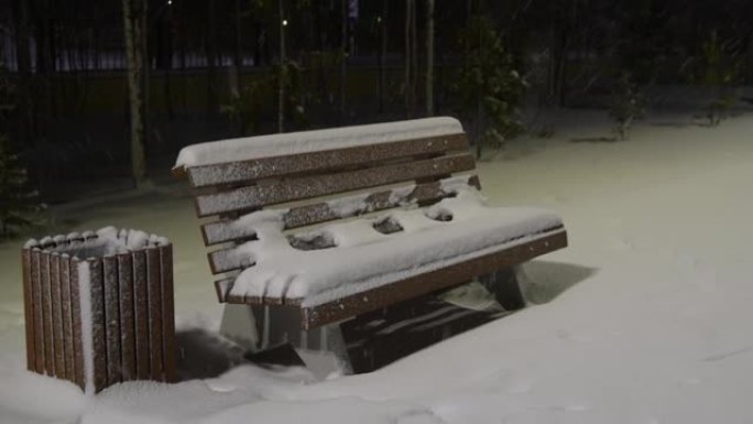 公园的冬夜在灯笼的灯光下在雪地里的长凳下雪了
