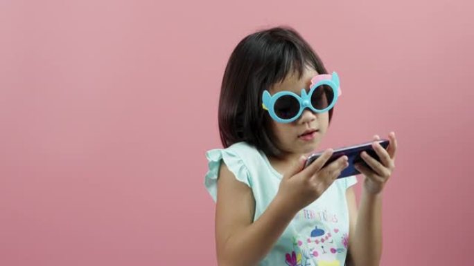 小女孩在粉色背景下用手机听音乐。