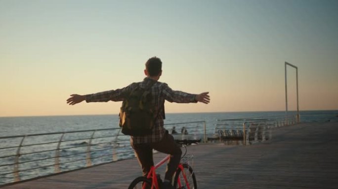 一个男人在海上日出时举起双手骑自行车的真实创意镜头。自由概念