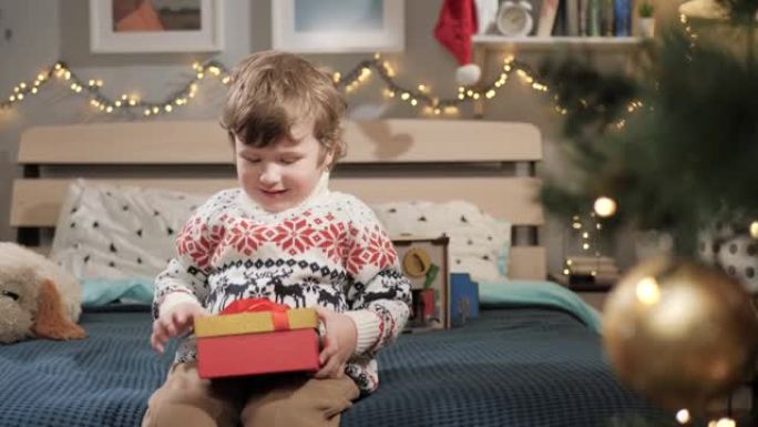 孩子打开圣诞礼物。2-3岁的婴儿坐在床上，打开圣诞礼物。慢动作