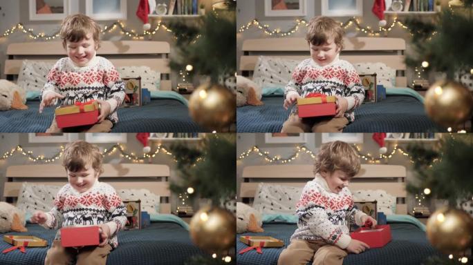 孩子打开圣诞礼物。2-3岁的婴儿坐在床上，打开圣诞礼物。慢动作