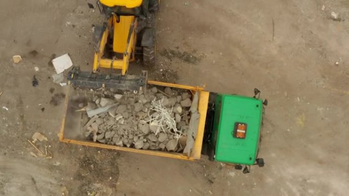 挖掘机正在建筑工地将建筑杂物装载到自卸车中。鸟瞰图。重建领土。拆除大楼。装修工作