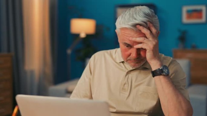 一个疲惫，破碎，辞职，全神贯注的老人坐在笔记本电脑，计算机前，用手盖脸。悲伤的高级商人沉迷于工作量