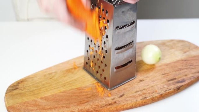 胡萝卜在切木板上的刨丝器上摩擦。