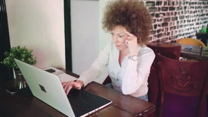 困惑和担心的女商人，试图解决问题，同时在自助餐厅使用笔记本电脑