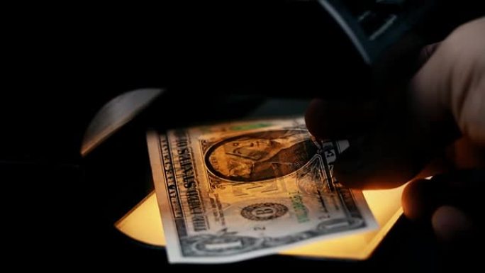 用验钞机检查美元钞票。探测钞票。假币。紫外线下的钱。钞票上的水印。