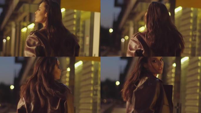 走在夜街上的黑发女人。穿着棕色夹克的时尚年轻漂亮模特在夜间城市背景4K时转向相机