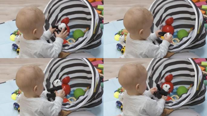 婴儿坐在地板上玩玩具储物篮里的玩具，可爱的7个月大的男婴在家里玩得很开心，探索他周围的新世界。
