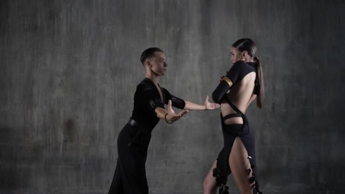 这对年轻的千禧一代舞蹈夫妇穿着黑色连衣裙，在工作室背景下以性感的姿势跳舞。