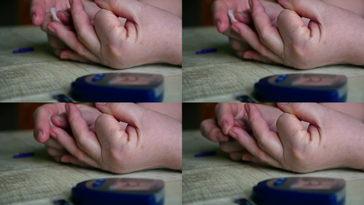 患有糖尿病的老年妇女在家中使用血糖仪测量和检查血糖。女人用棉絮止住手指上的血。一个血糖仪在桌子上。选
