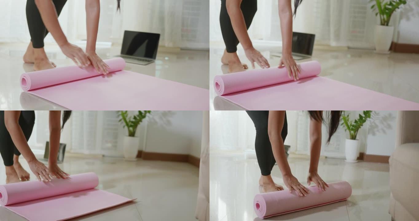 女人在运动准备工作之前或之后滚动粉红色瑜伽垫