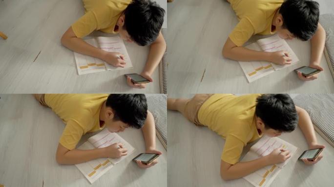 亚洲男孩躺在地板上做作业，同时在家学习在线课程，社交疏远的生活方式理念。