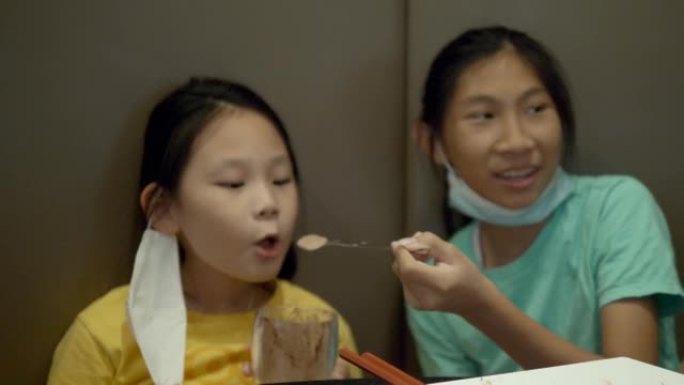 亚洲女孩在餐厅为姐姐喂巧克力冰淇淋圣代，生活方式概念。