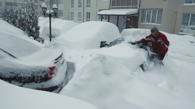 积雪和暴风雨。一名男子清理一辆冰雪覆盖的汽车。大雪。背包里的驾驶员用刷子清除了站在停车场上的汽车上的