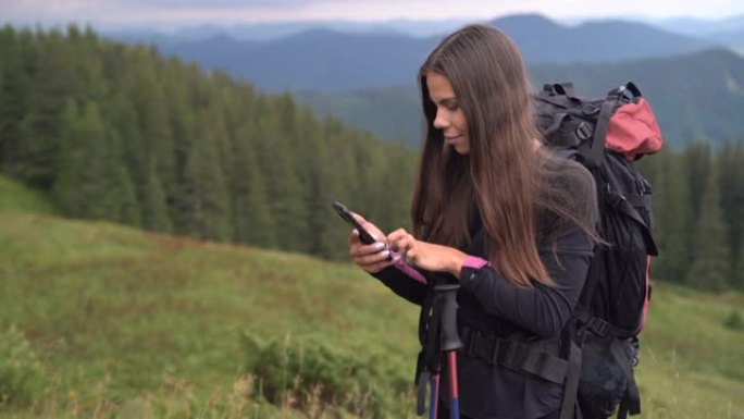 背着背包在山上的女孩旅行者在手机上的离线地图上制定了远足路线。森林附近的一名女性游客正在寻找前往营地