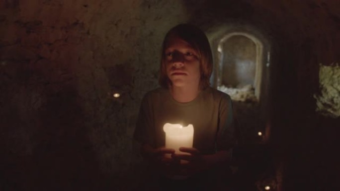 受惊的男孩带着蜡烛穿过黑暗的隧道