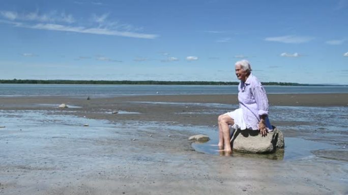 老年妇女独自夏天海滩放松坐石