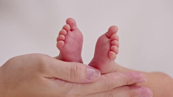母亲用爱心托着婴儿新生的脚。父母在舒适的家中手握着小巧的婴儿脚。舒适的心情和语气。母亲和新生婴儿护理